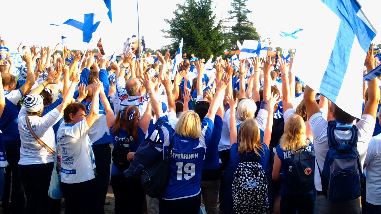 Sinivalkoisiin pukeutuneita lentopallofaneja kädet ylhäällä ja Suomen lippuja